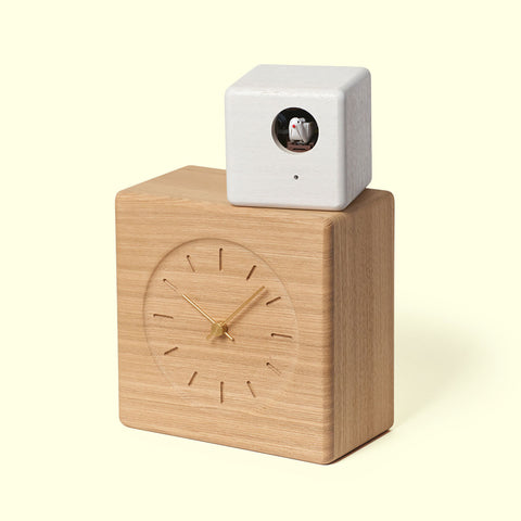 Lemnos Cubist Cuckoo clock with a wooden body, minimalist face and gold-tone hands, topped with a small white cube with circular opening that houses a cuckoo.