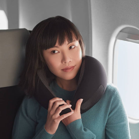 A model holding on to a midnight grey Ostrichpillow Go Neck Pillow while in flight