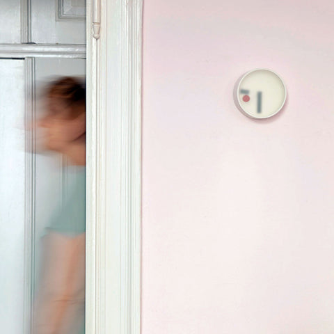 Kehai round wall clock with frosted face on a pink wall, beside a doorframe with a blurred figure passing through.