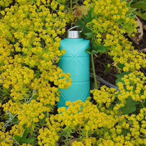 Scenic view of Difold Origami Bottle V2 in mint blue colour in a field of flowers