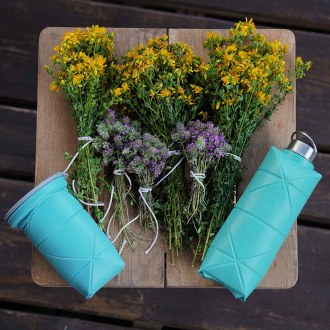 Scenic view of Difold Origami Bottle V2 in mint blue colour in a wooden setting with flowers