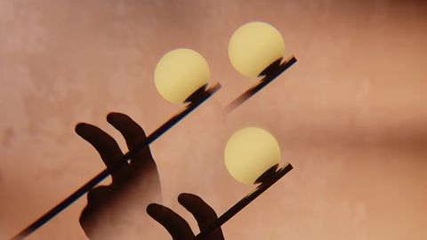 Close up of the Lumio Ovo lamp that shows the lit lamp in movement, with a dark hand silhouette against a warm peach-brown background.