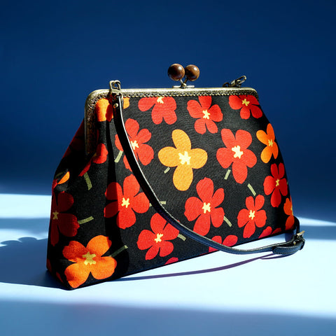 Cocoonese Clasp Sling Bag-White Rain Lily (Black): angled shot highlights hand-stitched frame, wooden clasps; wear crossbody or clutch, with inner zip