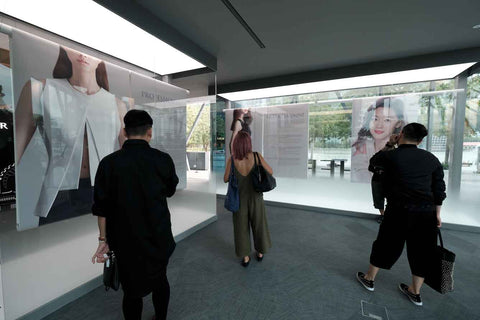 People observing exhibit panels behind glass, overlooking Marina Bay