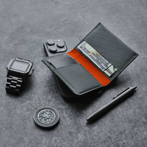 Ark Bifold Wallet X-PAC VX21: Slate Grey sits open among—phone, watch, pen—showcasing its sleek build, bold orange core, and easy access storage