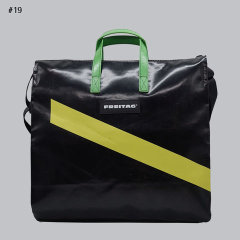 Front view of FREITAG F275 TILDA tote bag in black and yellow, with green handles and diagonal yellow stripe.