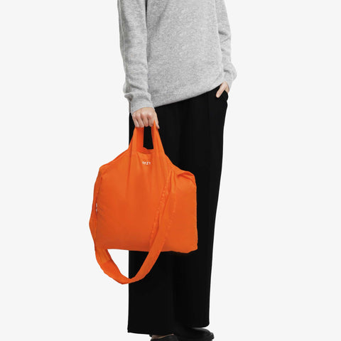 Model hand carrying a torii orange tetra tote bag