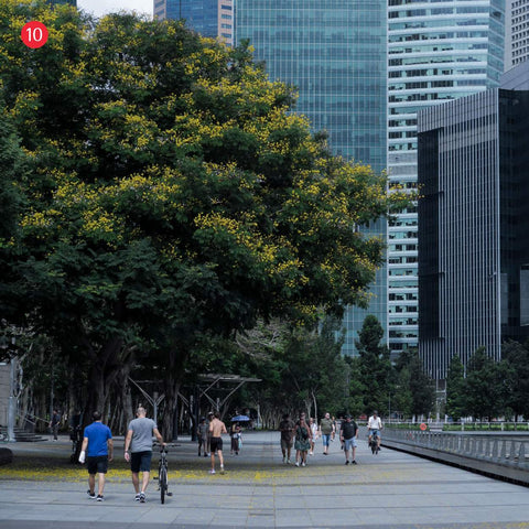 People walking and cycling along the Marina Bay waterfront promenade, with colourful trees and skyscrapers in the background