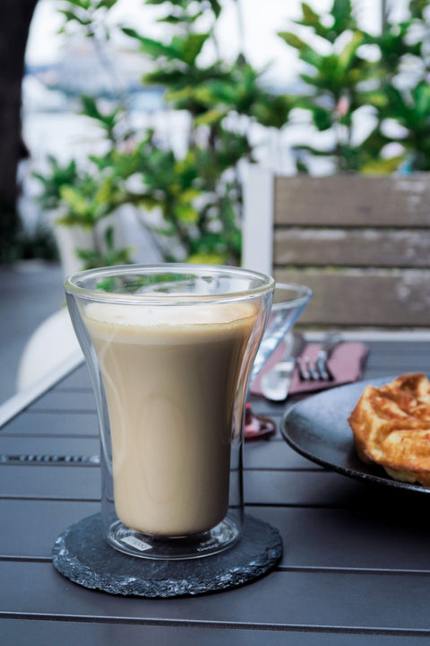 Outdoor seating with a hot coffee latte in double lining glass on a slate coaster with waffle and plants along Marina bay