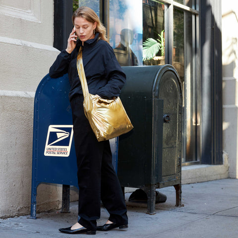 Model showcasing the bright glossy gold colour of Tetra tote bag with crossbody strap in an outdoor setting