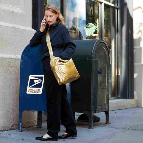 Model showcasing the bright glossy gold colour of Tetra tote bag with crossbody strap in an outdoor setting