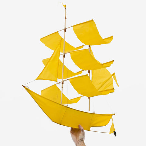 A model holding a canary yellow colour sailing ship kite with multiple sails, made of ripstop nylon and bamboo