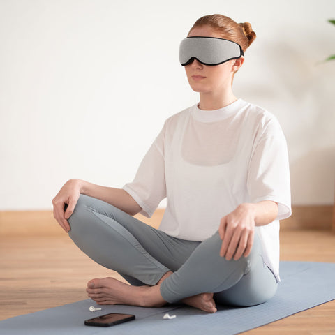 Ostrich Pillow Eye Mask in midnight grey worn by a woman meditating cross-legged on a yoga mat.