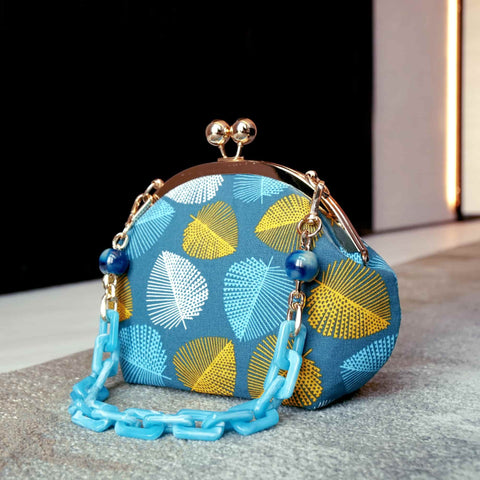 Coconeese Arcylic Chain Handle Clasp Sling Bag-Fall (Yellow Blue) styled outdoors, featuring leaf patterns in yellow and blue with a glossy chain