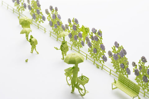 A close up view on the paper craft architectural model Rainy season with people in umbrellas and purple plants in silhouette at a 1/100 scale