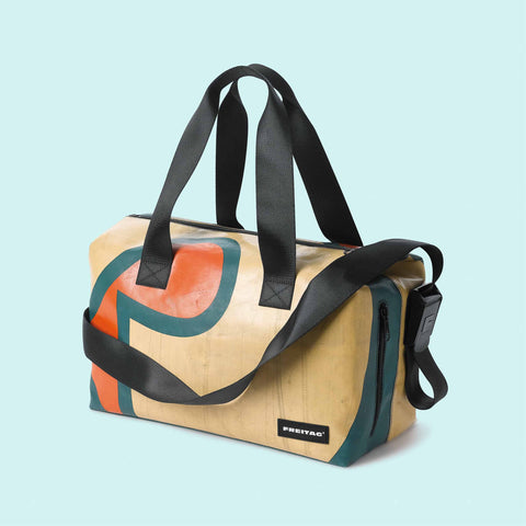 A FREITAG F45 LOIS Sports Bag with geometric pattern in beige, black, orange, and green colors, featuring a shoulder strap and handlebar