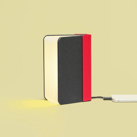 Side view of Lumio Lito mini book lamp partially open with warm light while plug in as a charger for phone