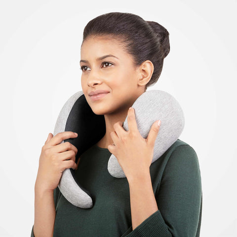 A model putting on a midnight grey Ostrichpillow Go Neck Pillow