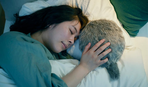 A women lying in bed sleeping while holding petit Qoobo providing companionship and comforts