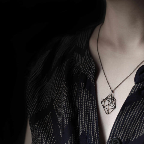 Model wears the Moorigin Stainless Steel Pendant - Stone S at mid-chest, its bold geometric form contrasting elegantly with a dark patterned top