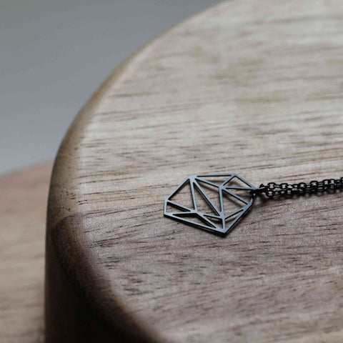 Stainless Steel Pendant - Stone XS rests on a wooden surface, showcasing its clean geometric lines and sleek, minimal design in close-up