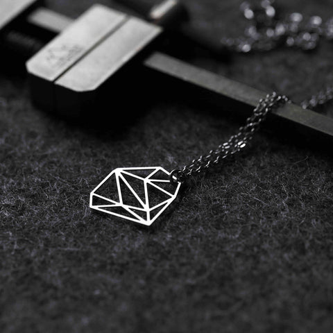 Stainless Steel Pendant - Silver XS rests on textured fabric, its geometric form contrasted by industrial tools for a sleek, modern edge