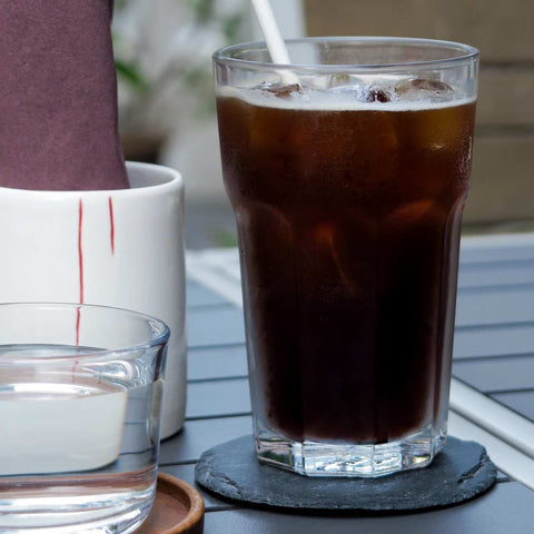 Glass of iced black coffee with a straw and a glass of water at design museum shop outdoor seating
