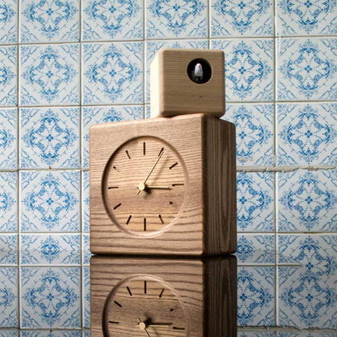 Lemnos Cubist Cuckoo Clock, wooden cube body with a small cuckoo housing on top, against blue and white patterned tiles.