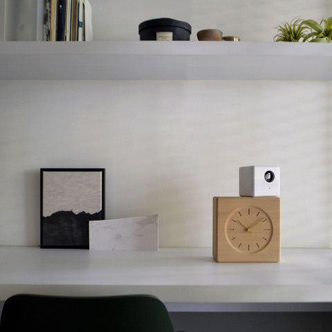 Wooden Cubist Cuckoo Clock with white cuckoo cube on top, styled on a shelf with framed art and books.