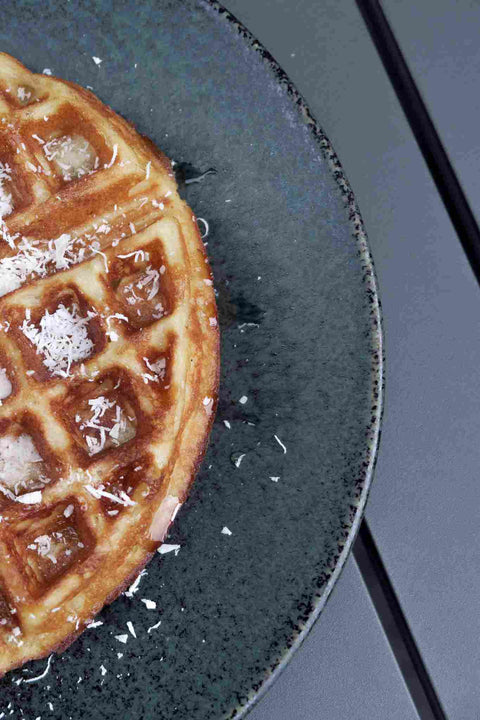 Waffle with syrup and coconut shavings on a dark plate