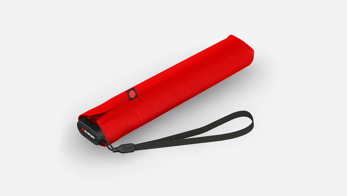 A red Knirps US.050 Ultra Light Slim Manual Umbrella with a black wrist strap and a small black logo, shown on a clean light gray background.