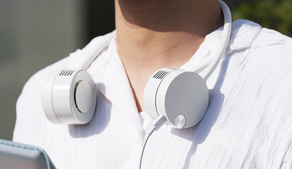 Lumena Fan Pro Duo neck fan with round ear cups worn around a person's neck, shown in a close-up outdoor shot.