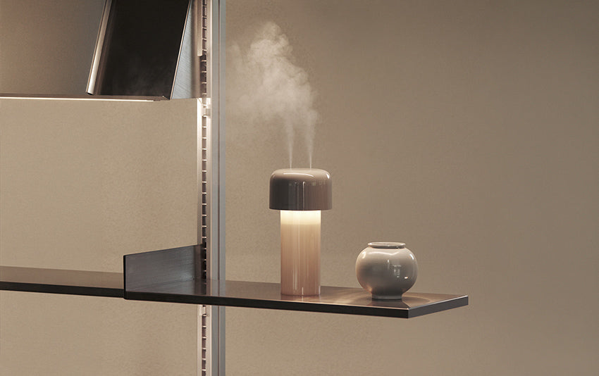 Lumena Mist Stand humidifier and lamp with rising mist, displayed on a floating shelf next to a small grey ceramic vase against a beige wall.