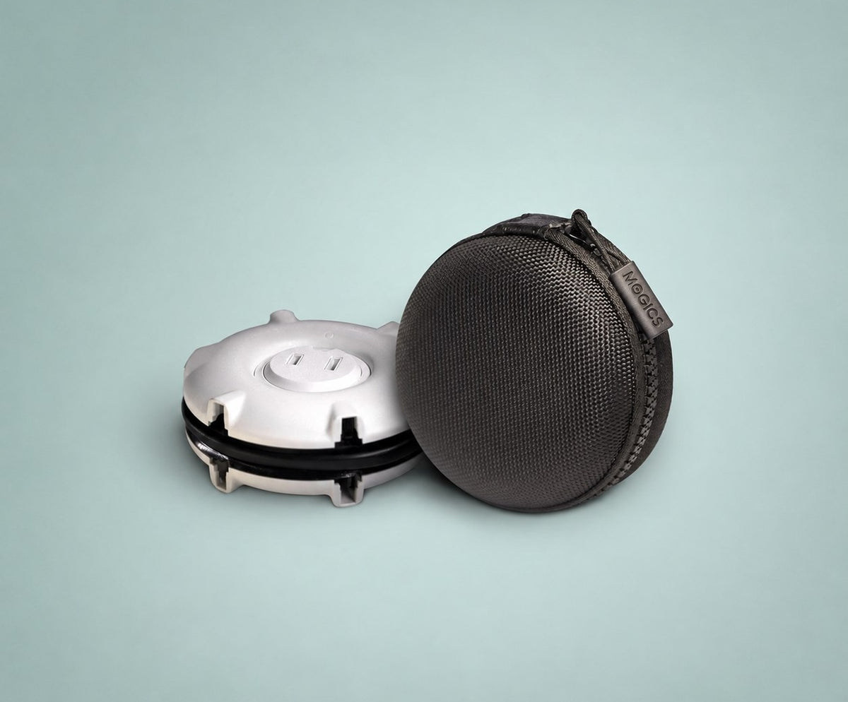 A white, round, compact Mogics travel adapter and power strip shown with its grey textured fabric sleeve with a zipper. The closed sleeve features a small leather tag with the brand name 'MOGICS'