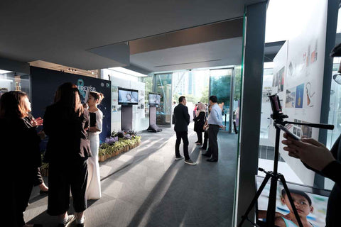 Evening sun ray from Marina bay illuminating into gallery exhibit space, with backdrops and portable screens behind groups of people gathering