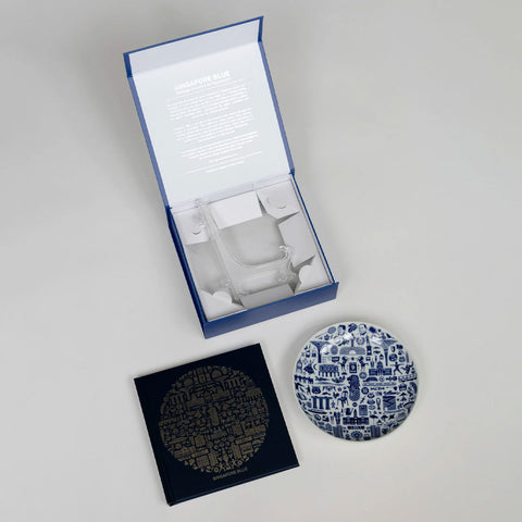 Blue box with a booklet and a Supermama porcelain plate on a grey background
