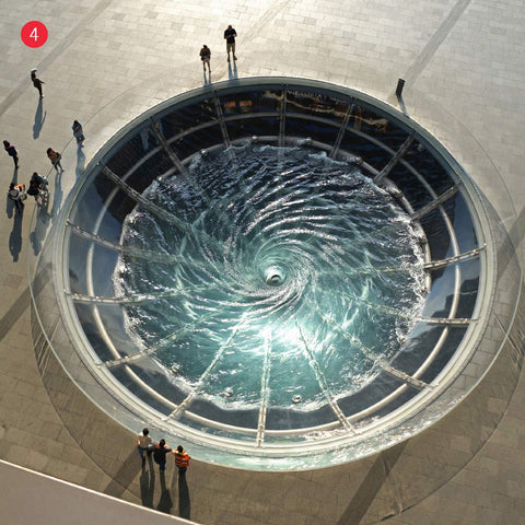 Visitors gathered around observing a large circular water feature with whirlpool installation at Marina bay 
