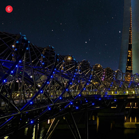 Iconic helix bridge with spiralling blue lighting surrounding a walkway above Marina bay under a starry night sky