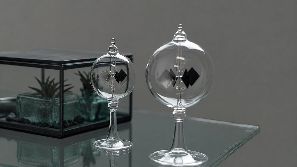 Two clear glass Hightide radiometers on a reflective glass surface, with a terrarium in the background.