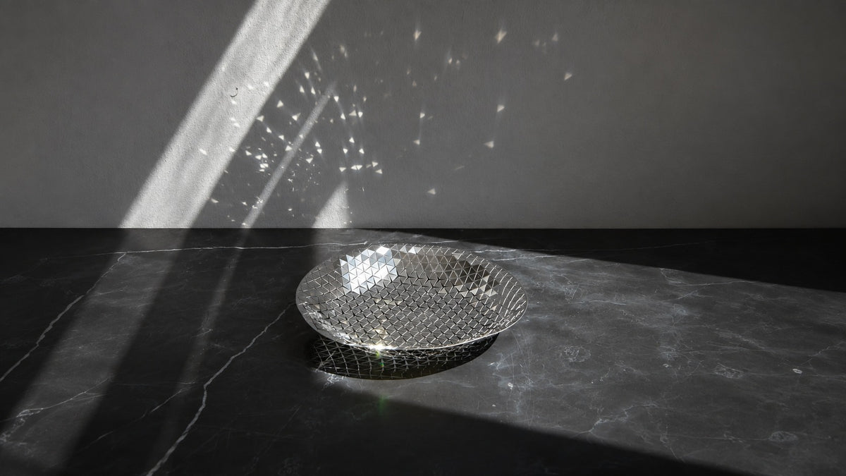 A clear, textured Fundamental Berlin Push bowl with a honeycomb pattern sits on a dark marble surface under dramatic diagonal sunlight casting shadows and sparkles across the scene.