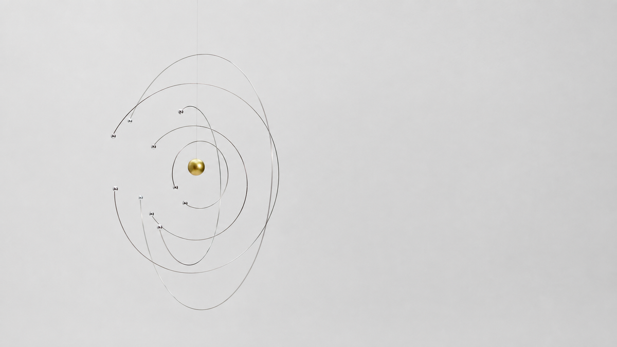 A minimalist wall hanging Flensted Niels Bohrs hanging mobile featuring a small gold sphere suspended in the center by thin black concentric rings on a light gray wall.